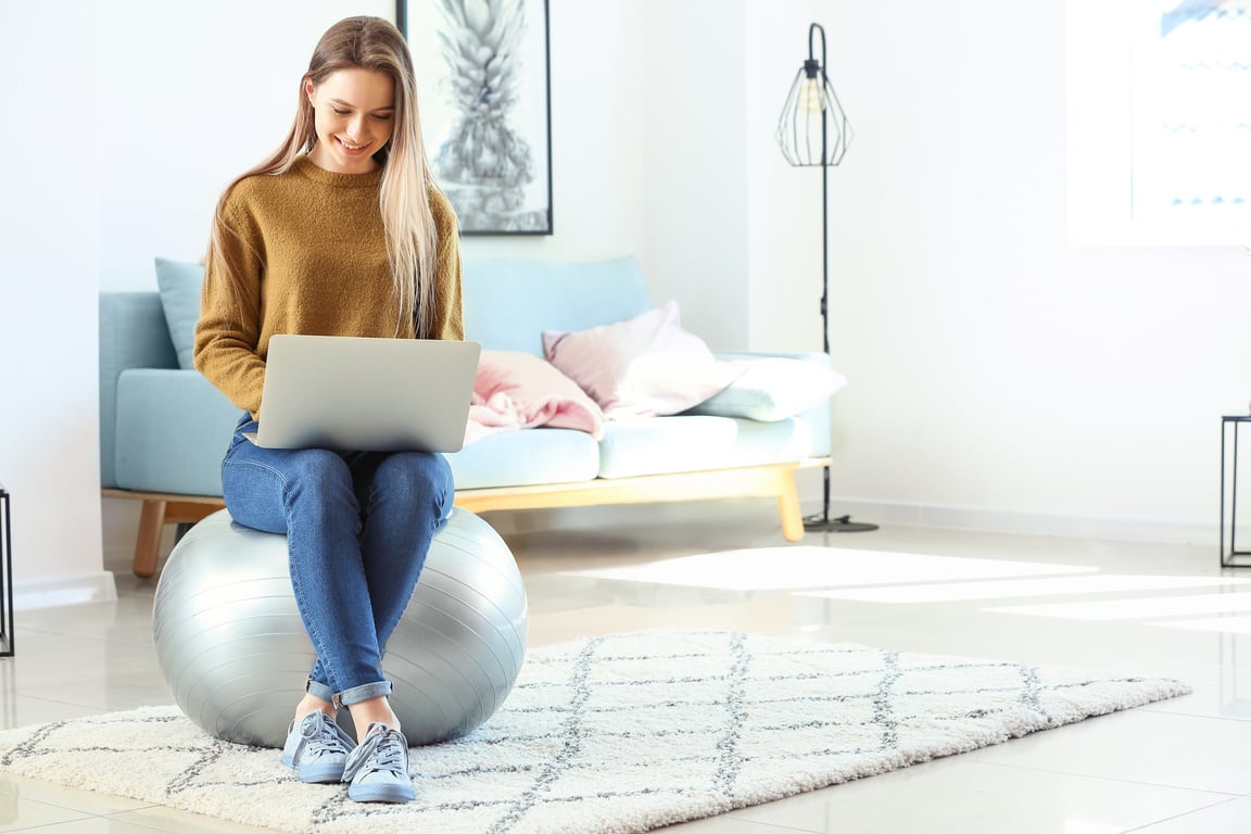 Young Woman with Laptop Sitting on Fitball at Home